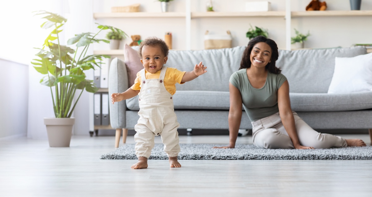 Baby boy taking his first steps at home with his mother.